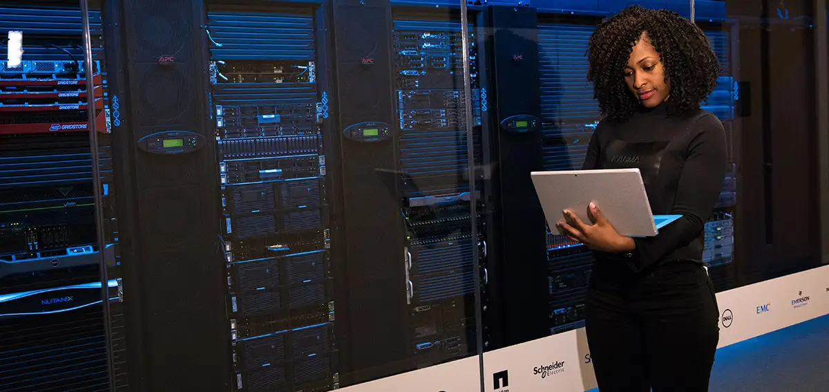 African American Woman holding laptop in front of web servers